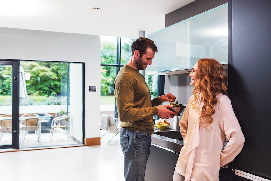 a couple stand in a kitchen preparing a meal, listening to music powered by Crestron Home