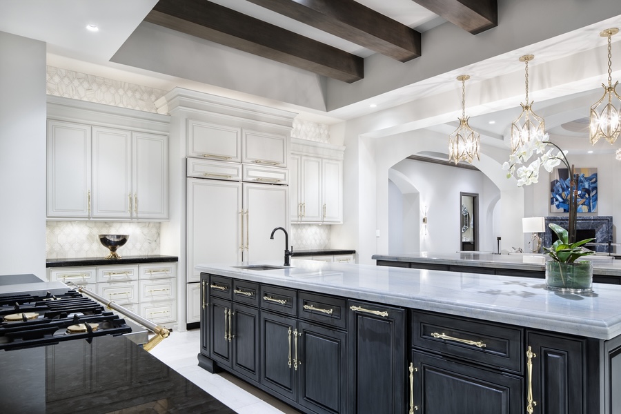 A grandiose kitchen with white cabinets and countertops is illuminated with Lutron smart lighting