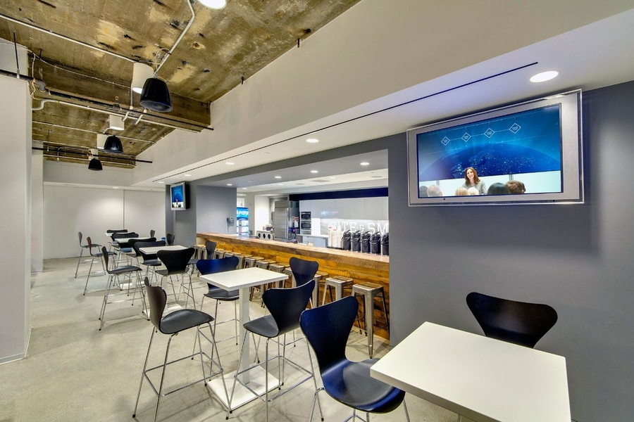 Modern cafeteria with exposed ceiling, wall-mounted TV, and in-ceiling speakers.